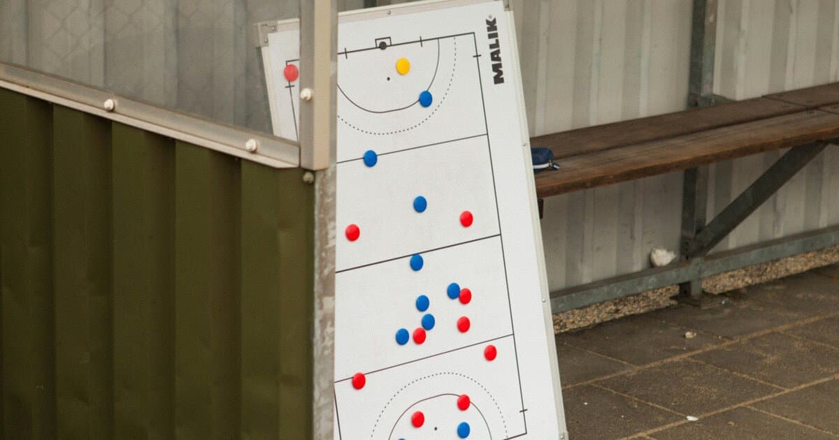 Physical tactical board with magnetic player pieces leaning against a dugout bench at a football pitch