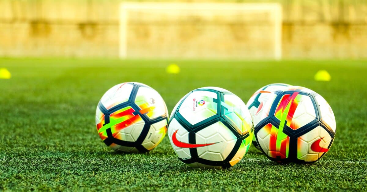 Colorful footballs on a training pitch with cones and goal in the background, ready for practice drills